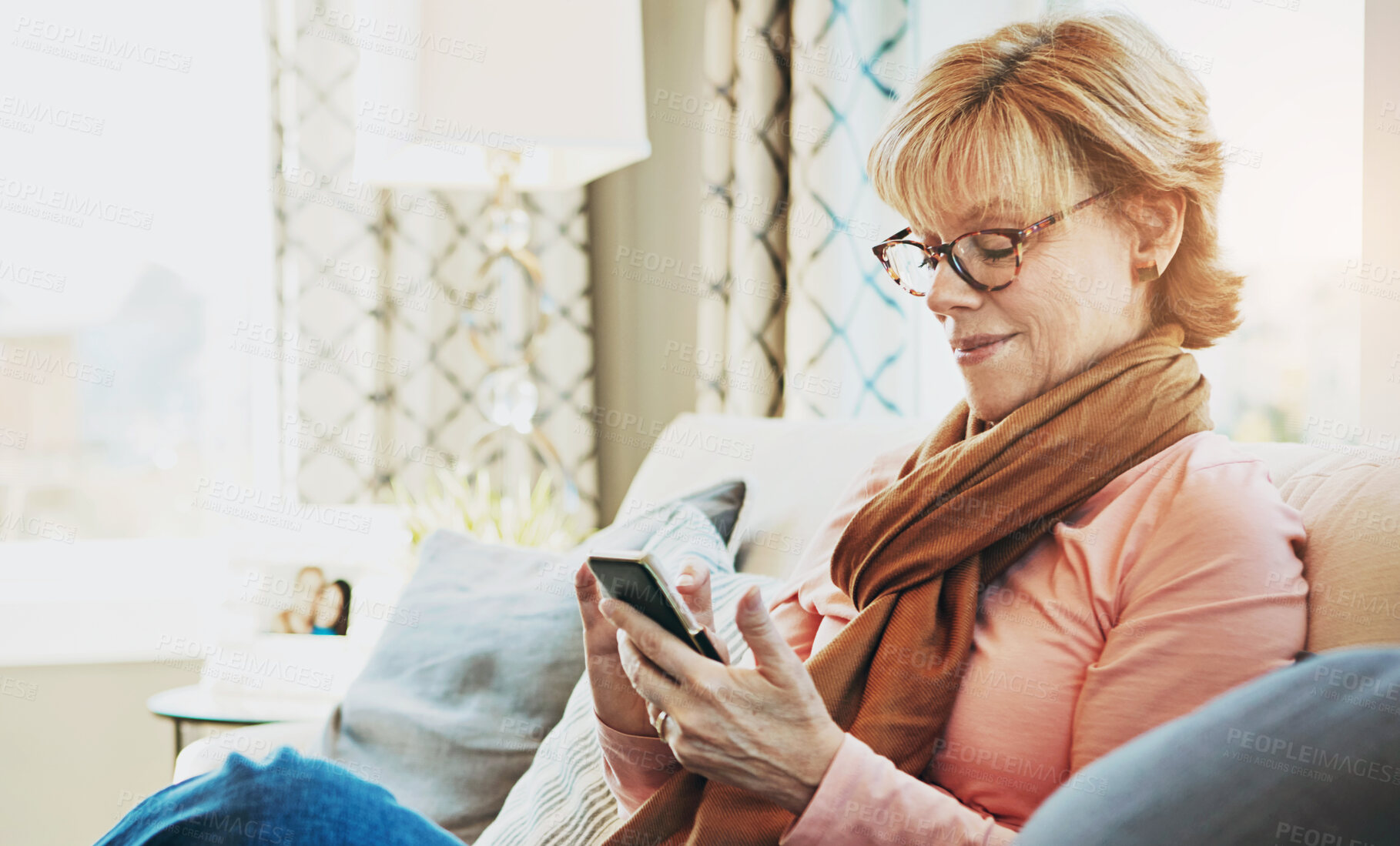 Buy stock photo Shot of a mature woman using a phone at home on the sofa