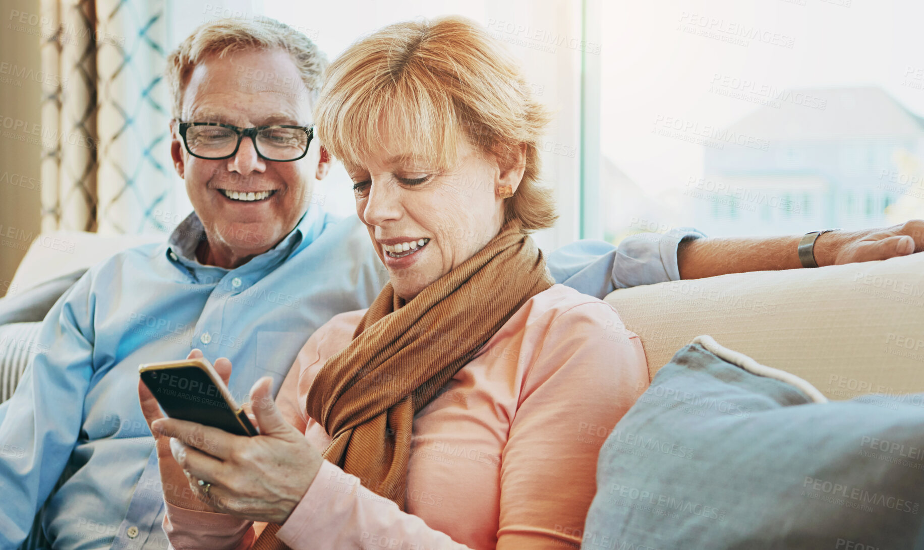 Buy stock photo Shot of a mature couple using a phone together at home on the sofa