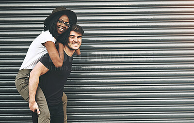 Buy stock photo Fun, trendy and happy interracial couple enjoying a piggyback ride together outside against an urban background. Lovers bonding and being playful. Smiling and relaxing while walking outdoors