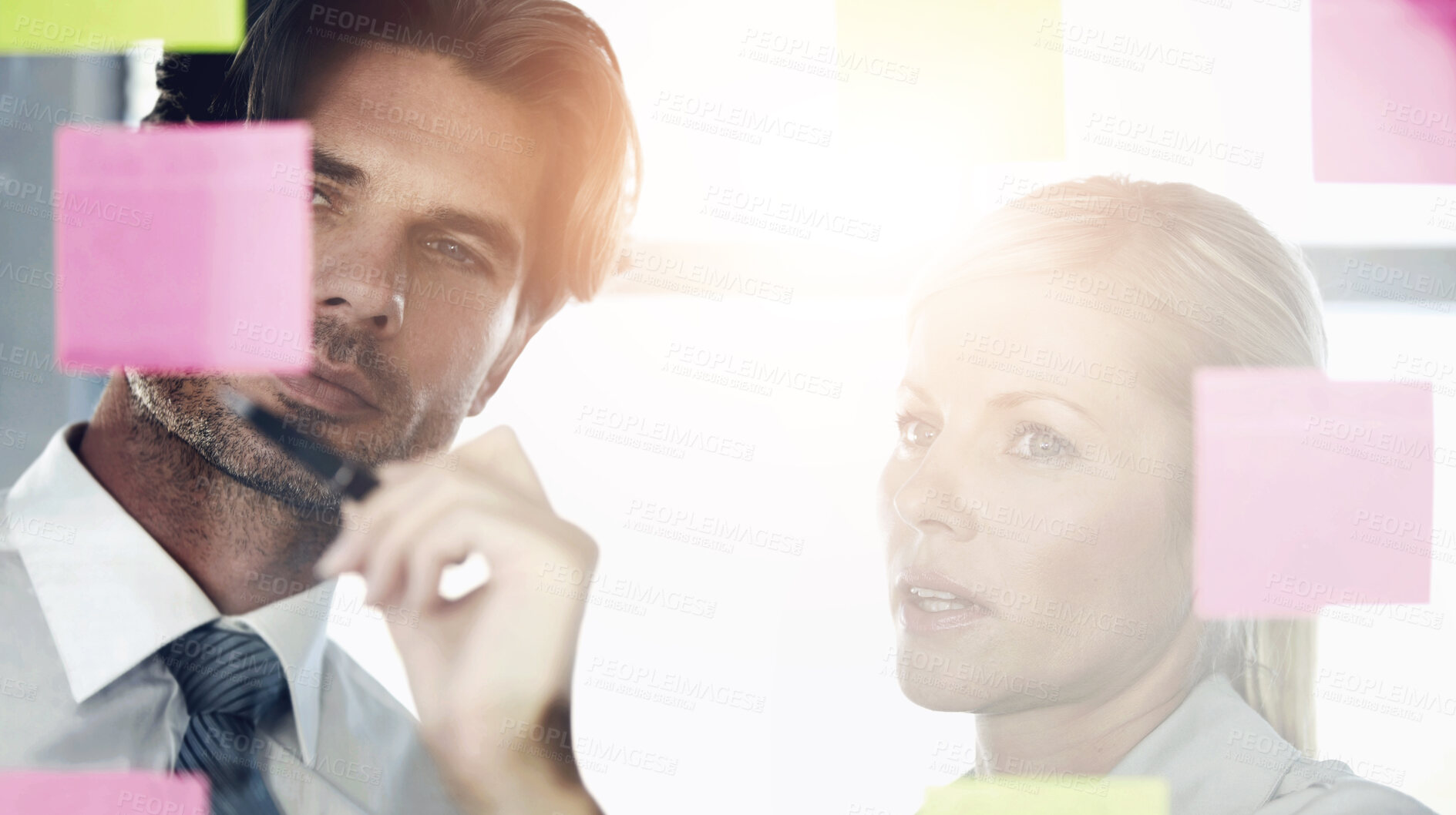 Buy stock photo A man and woman in the office looking at notes on a glass window, discussing and deciding