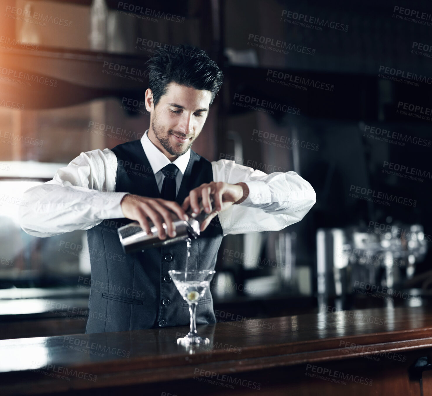 Buy stock photo A handsome young bartender mixing a cocktail for a customer