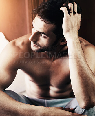 Buy stock photo Sexy young man sitting on the edge of his bed deep in thought