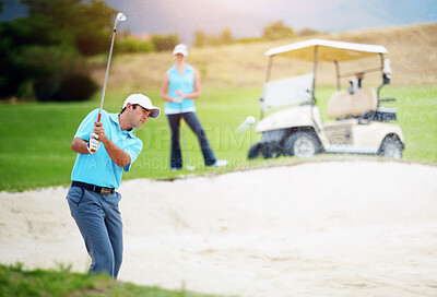 Buy stock photo A young male golfer chipping his ball out of a bunker while his female partner looks on from the fairway