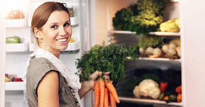 Buy stock photo Smiling woman adding some fresh carrots to her fridge already stocked with raw vegetables