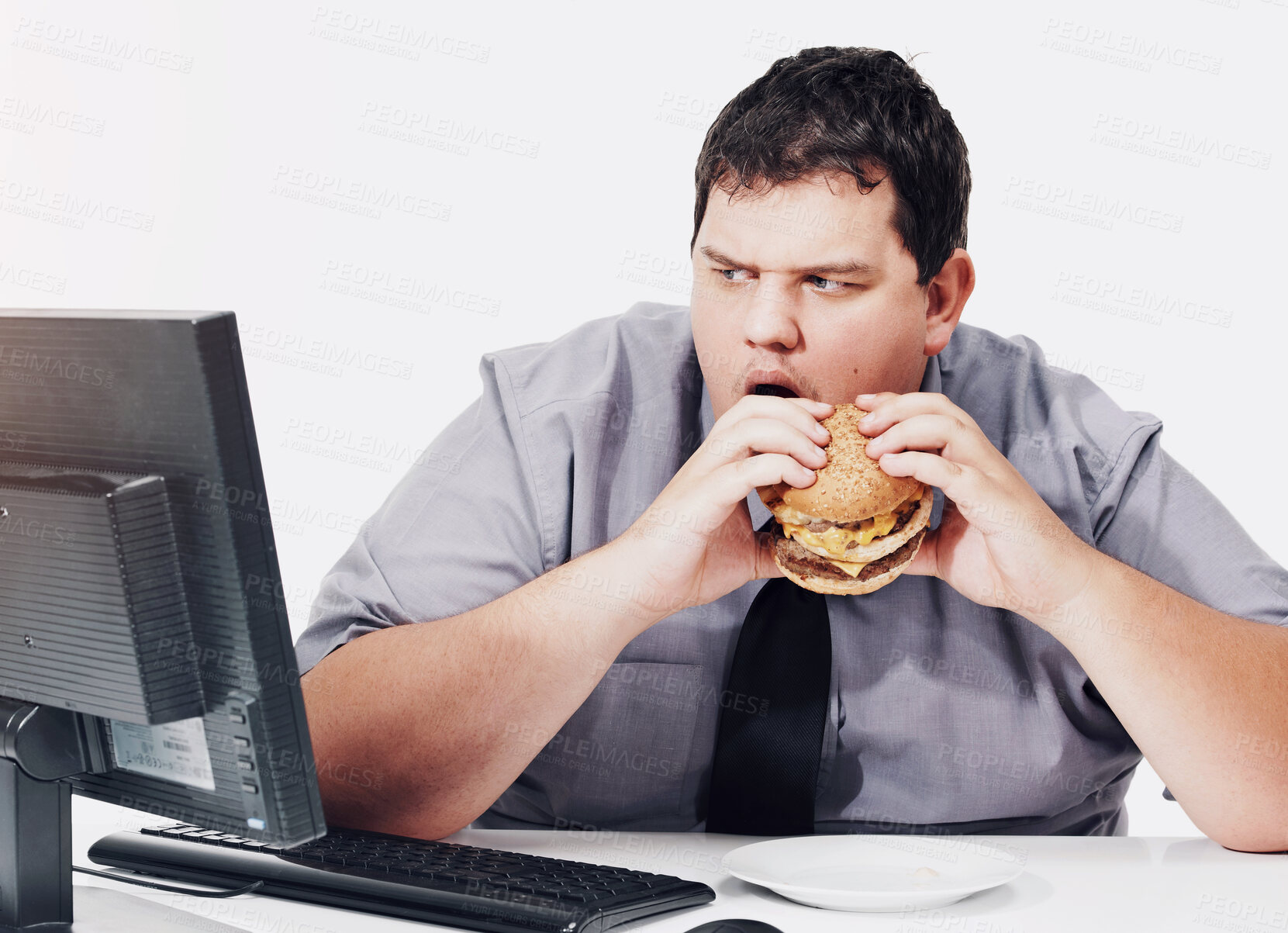 Buy stock photo A young man eating his lunch at his desk at work while staring with mouth agape at his monitor - unhealthy eating habits