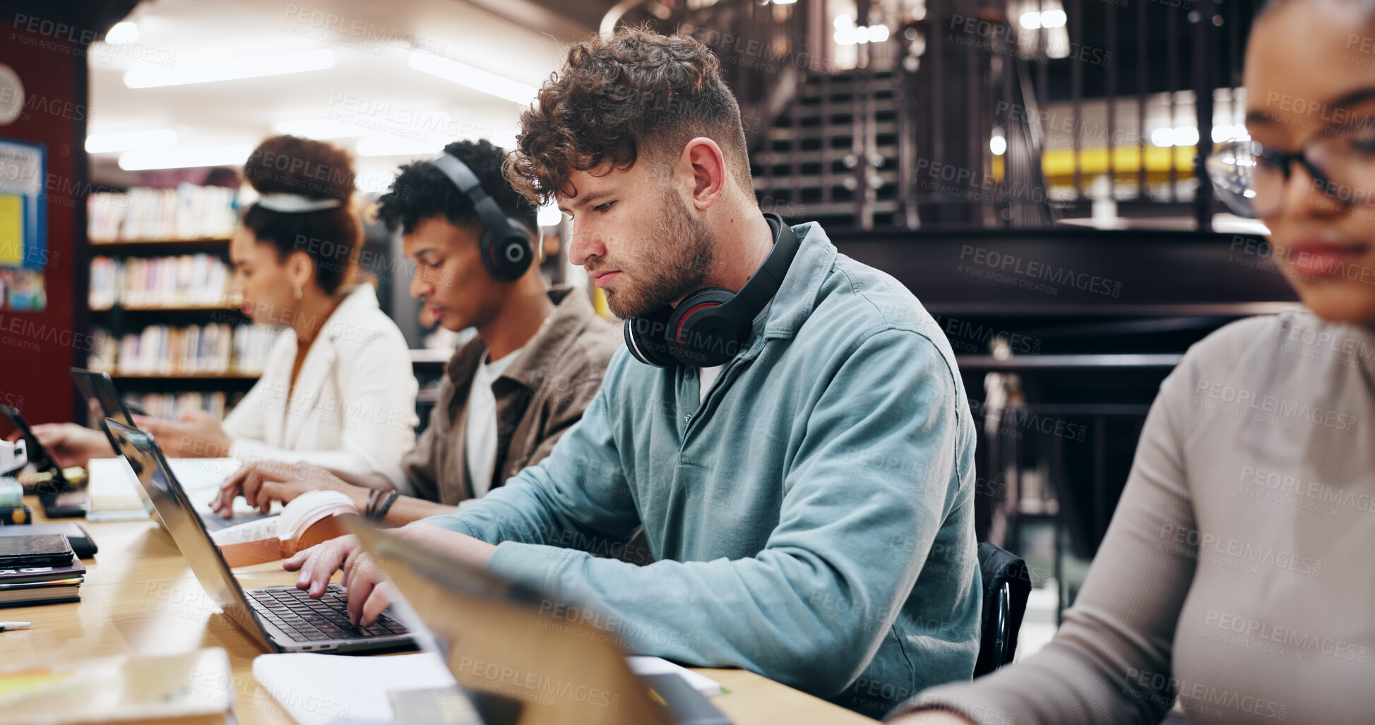 Buy stock photo Man, studying and laptop in library for education, problem solving and working on research assignment. Student group, headphones and computer at college for learning, online course and productivity