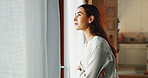 Woman, arms crossed and thinking by window in living room with daydreaming, reflection and memory in home. Girl, person and thoughtful in lounge with wondering, check weather and nostalgia with relax