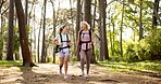 Mother, daughter and walking in forest with laughing for fitness adventure, sightseeing and explore nature. Backpack, mature woman and girl in woods with hiking, holiday travel and bonding with joke