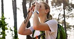 Woman, backpack and trekking with binoculars in forest for bird watching, sightseeing or outdoor discovery in nature. Female person, tourist or hiker with vision for tourism, hiking or observation