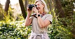 Travel, camera and mature woman in forest for adventure guide, wildlife photography or trekking. National park, environment and birdwatching with person hiking in nature for field research or explore