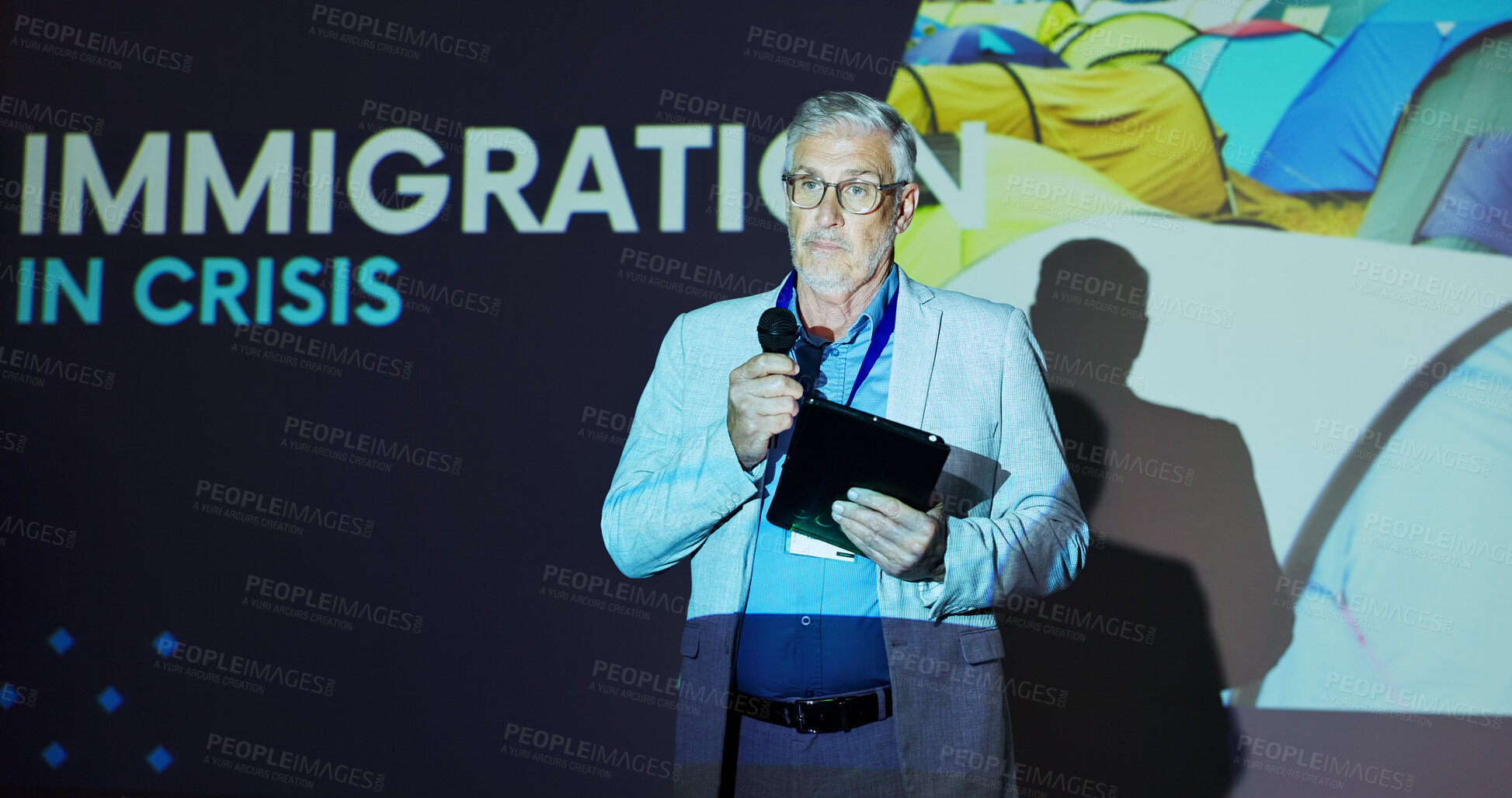 Buy stock photo Seminar, speaker and man on stage for global immigration presentation with microphone, tablet and information. Ideas, change and mature presenter at screen for international refugee crisis conference