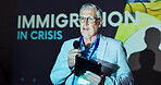 Seminar, speaker and man at screen for global immigration presentation with microphone, tablet and information. Ideas, change and mature presenter at podium for conference on world refugee crisis