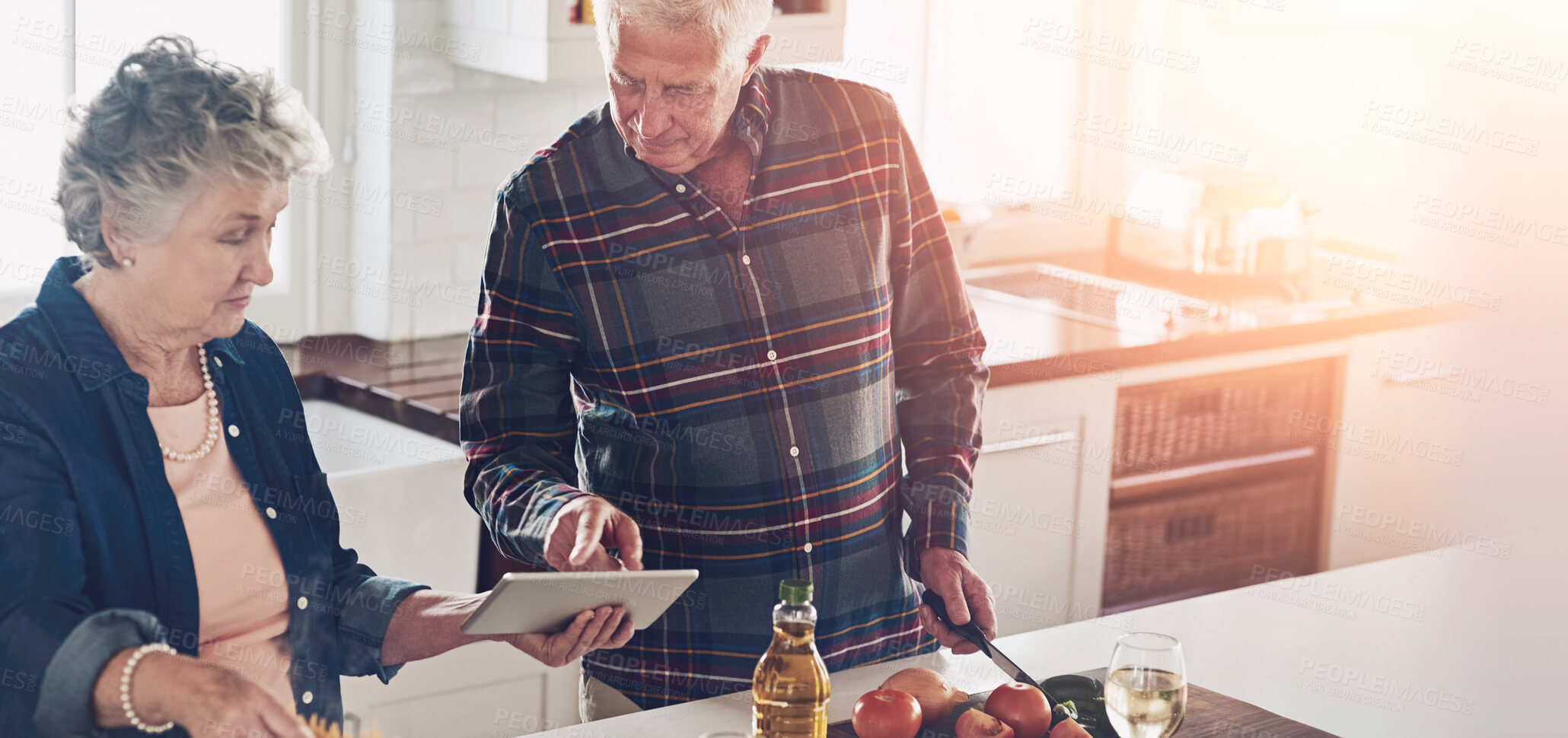 Buy stock photo Cropped shot of a senior couple using a digital tablet while cooking together in their kitchen at home