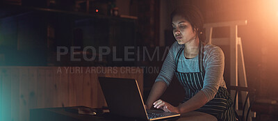 Buy stock photo Shot of a young entrepreneur working late on a laptop in a workshop