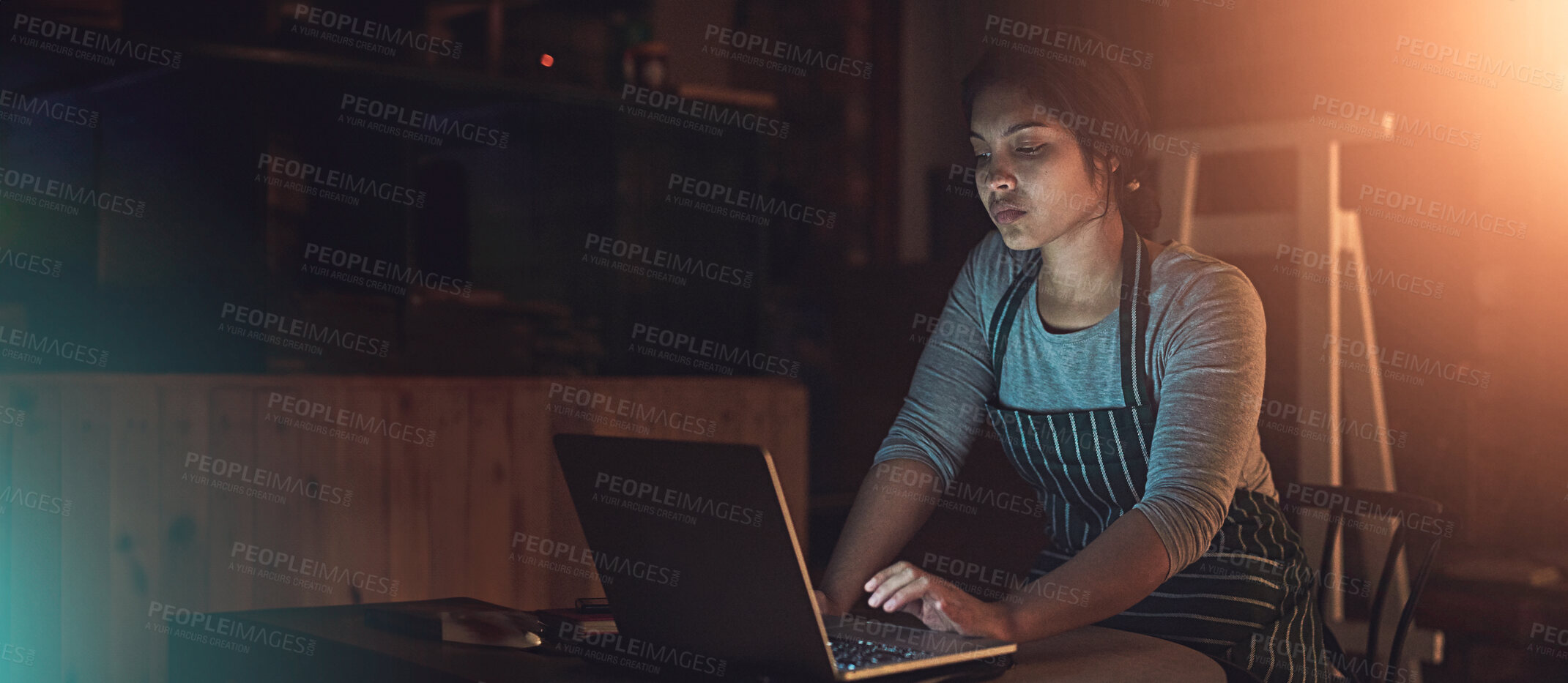 Buy stock photo Shot of a young entrepreneur working late on a laptop in a workshop