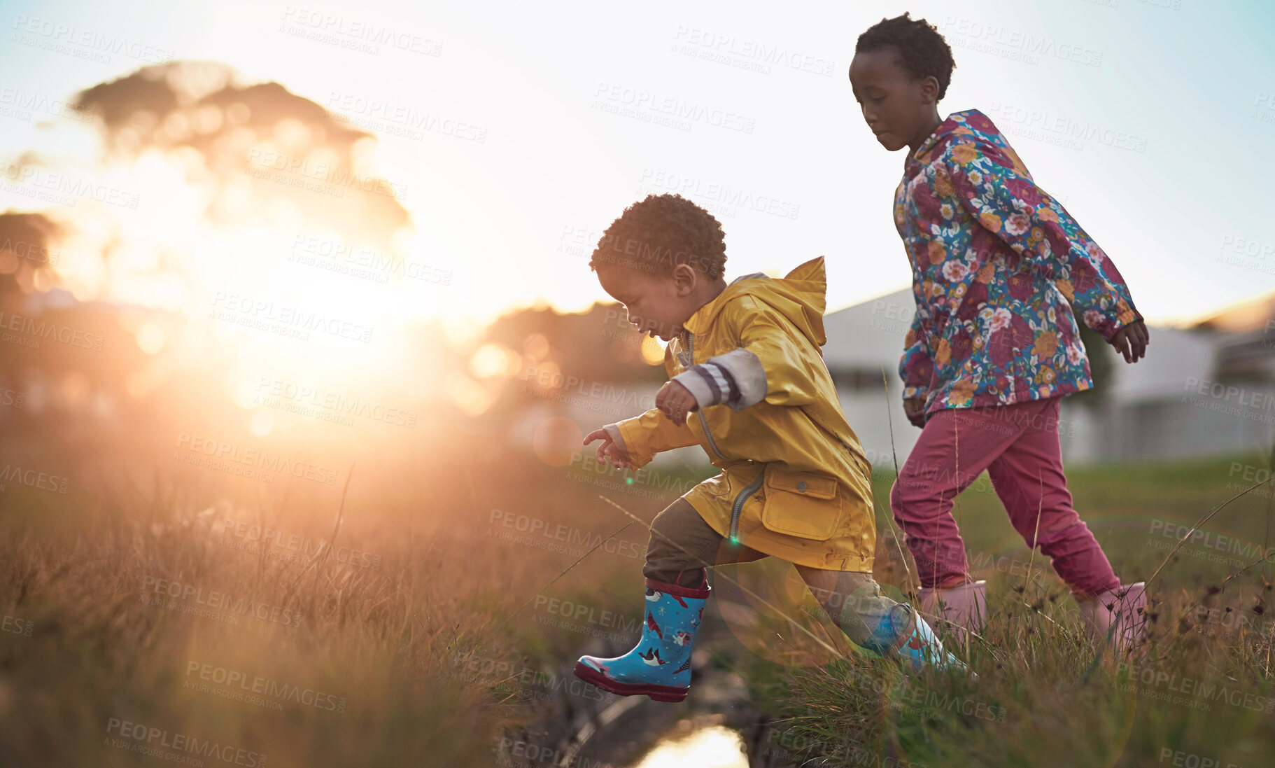 Buy stock photo Shot of a brother and sister jumping over water while playing outside