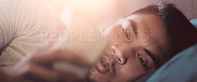 Buy stock photo Shot of a young man looking at his phone while lying in bed