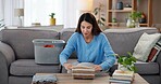 Laundry, folding and woman on sofa with care, washing basket and home management in living room. Housekeeping, chores and happy housewife on couch sorting fresh clothes, cleaning and morning routine