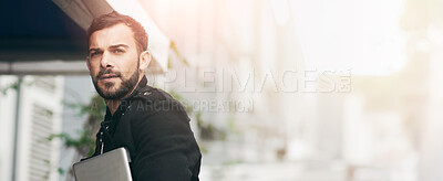 Buy stock photo Shot of a handsome young man carrying his phone and laptop while out in the city