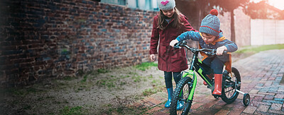 Buy stock photo Girl, siblings and teaching with bicycle for ride, training wheels or hobby in outdoor activity in neighborhood. Little child or kid helping young brother on bike for playful cycling or trip at park