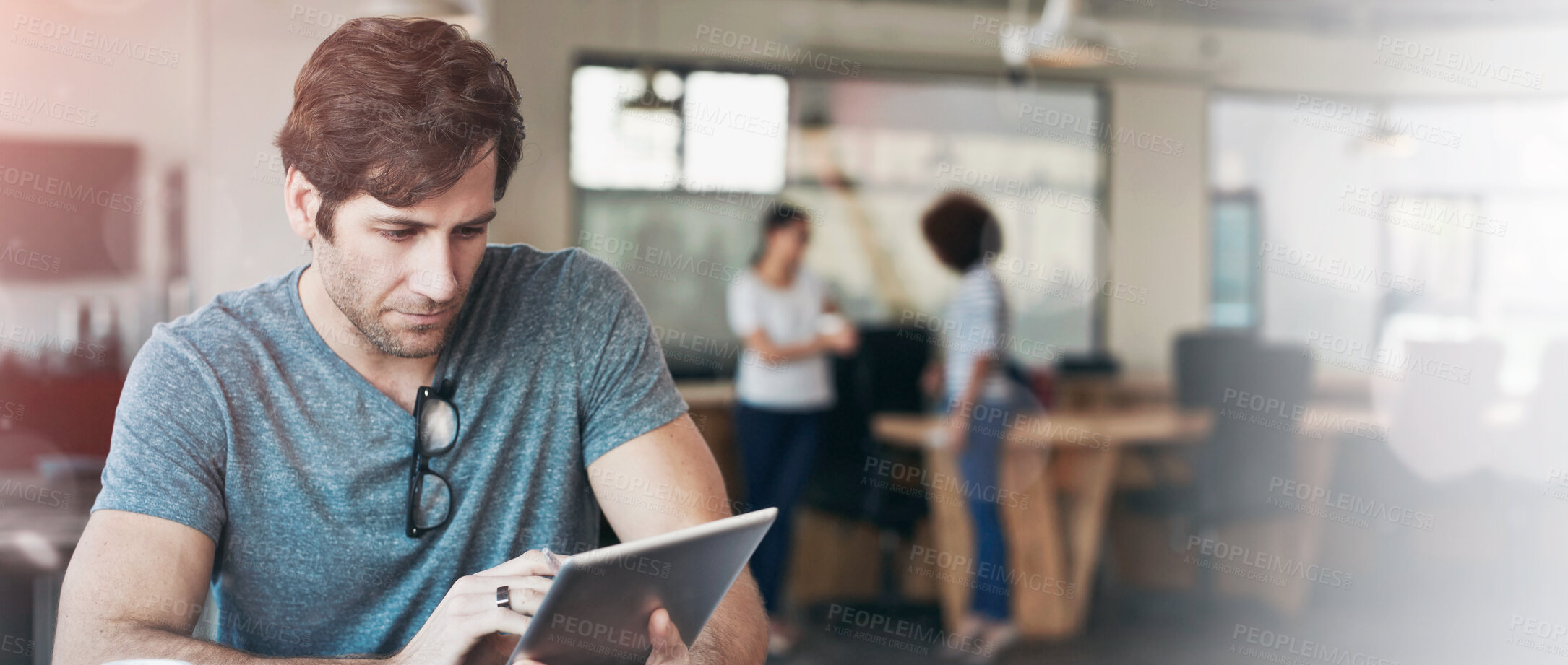 Buy stock photo Shot of a young man working on a digital tablet in an office