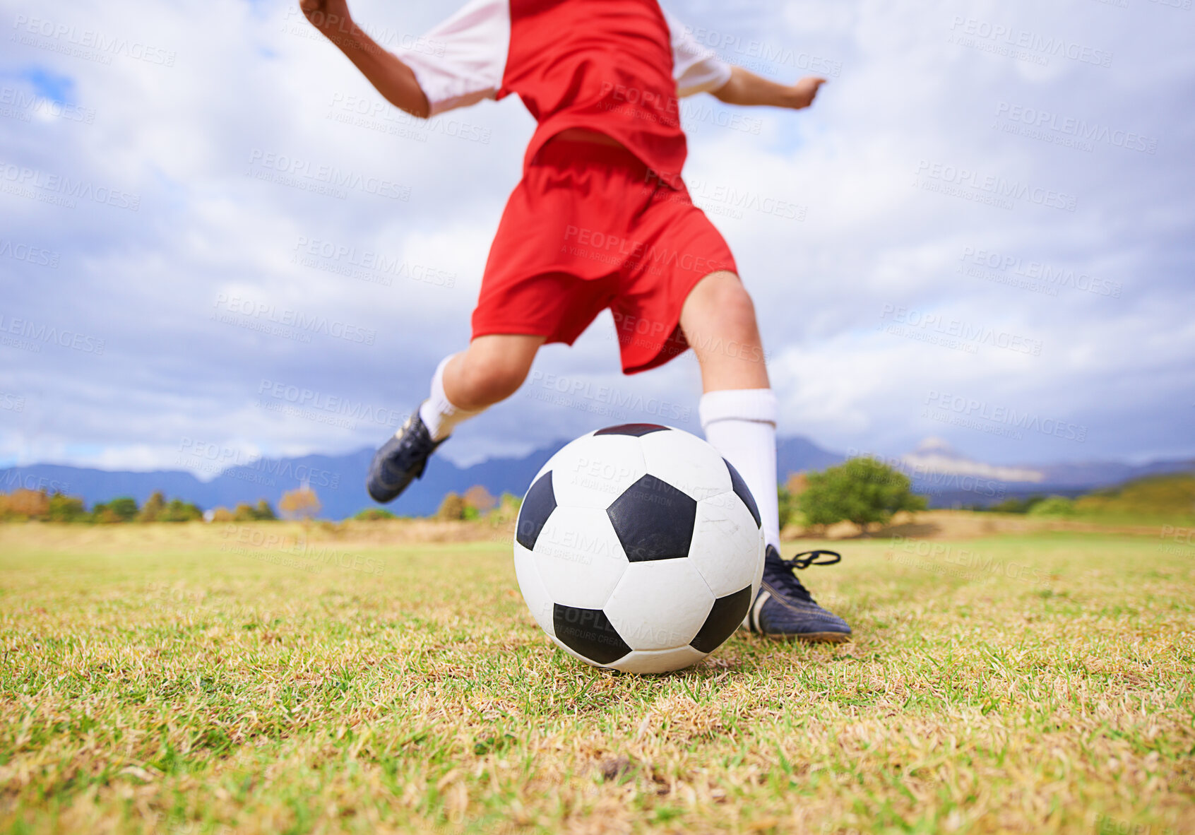 Buy stock photo Child, kicking and soccer ball on green grass for sports, training or practice with clouds and blue sky. Closeup of football player foot ready for kick off, game or match on outdoor field in nature