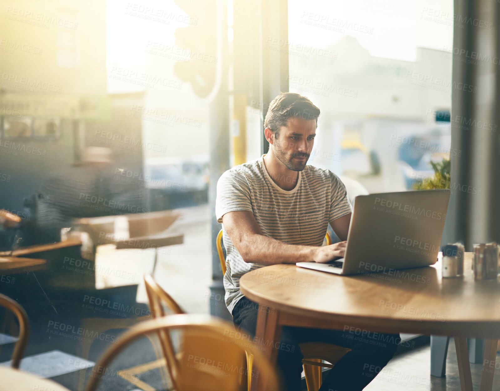 Buy stock photo Shot of a young man working on his laptop in a coffee shop