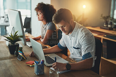 Buy stock photo Shot of a young designer working late with his colleague blurred in the background