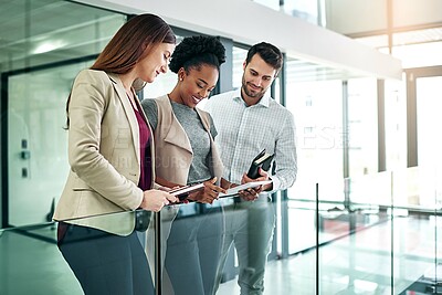 Buy stock photo Shot of a group of colleagues talking together over a digital tablet while standing in a large modern office