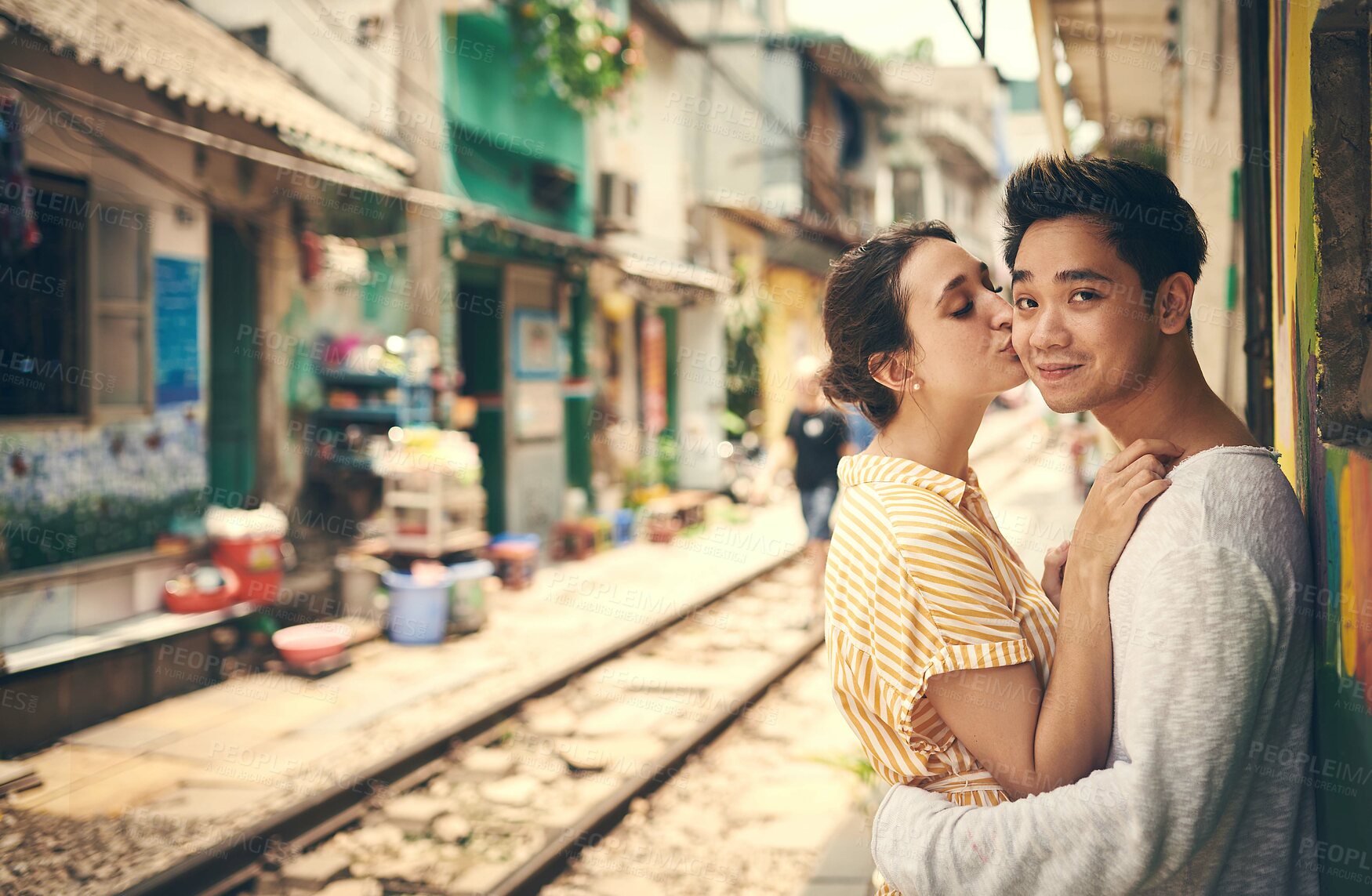 Buy stock photo City, railway and couple with kiss for hug, travel adventure and explore vacation for anniversary. Interracial marriage, woman and man in portrait for admiration, love and bonding outdoor in Vietnam