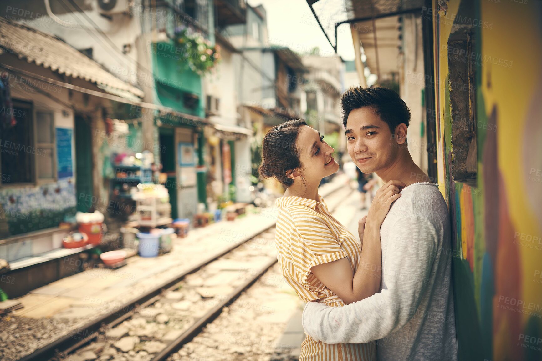 Buy stock photo City, railway and couple in portrait for hug, travel adventure or explore vacation for anniversary. Interracial marriage, woman and man with romance for admiration, love or bonding outdoor in Vietnam