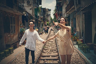 Buy stock photo Happy couple, holding hands and point in city for travel, sightseeing or healthy relationship with trust. Man, woman or excited on Vietnam railway with direction, affection or date outing on journey