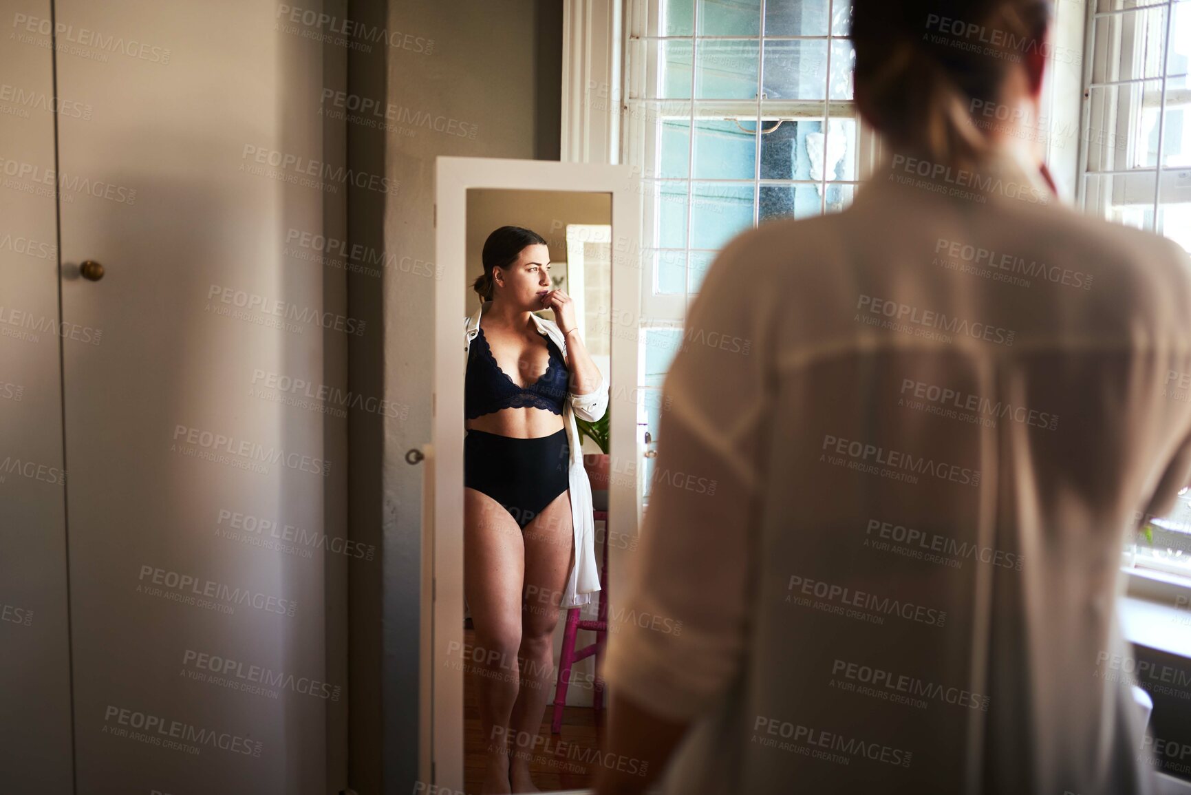 Buy stock photo Cropped shot of an attractive young woman looking thoughtful while standing in front of the mirror in her bedroom at home