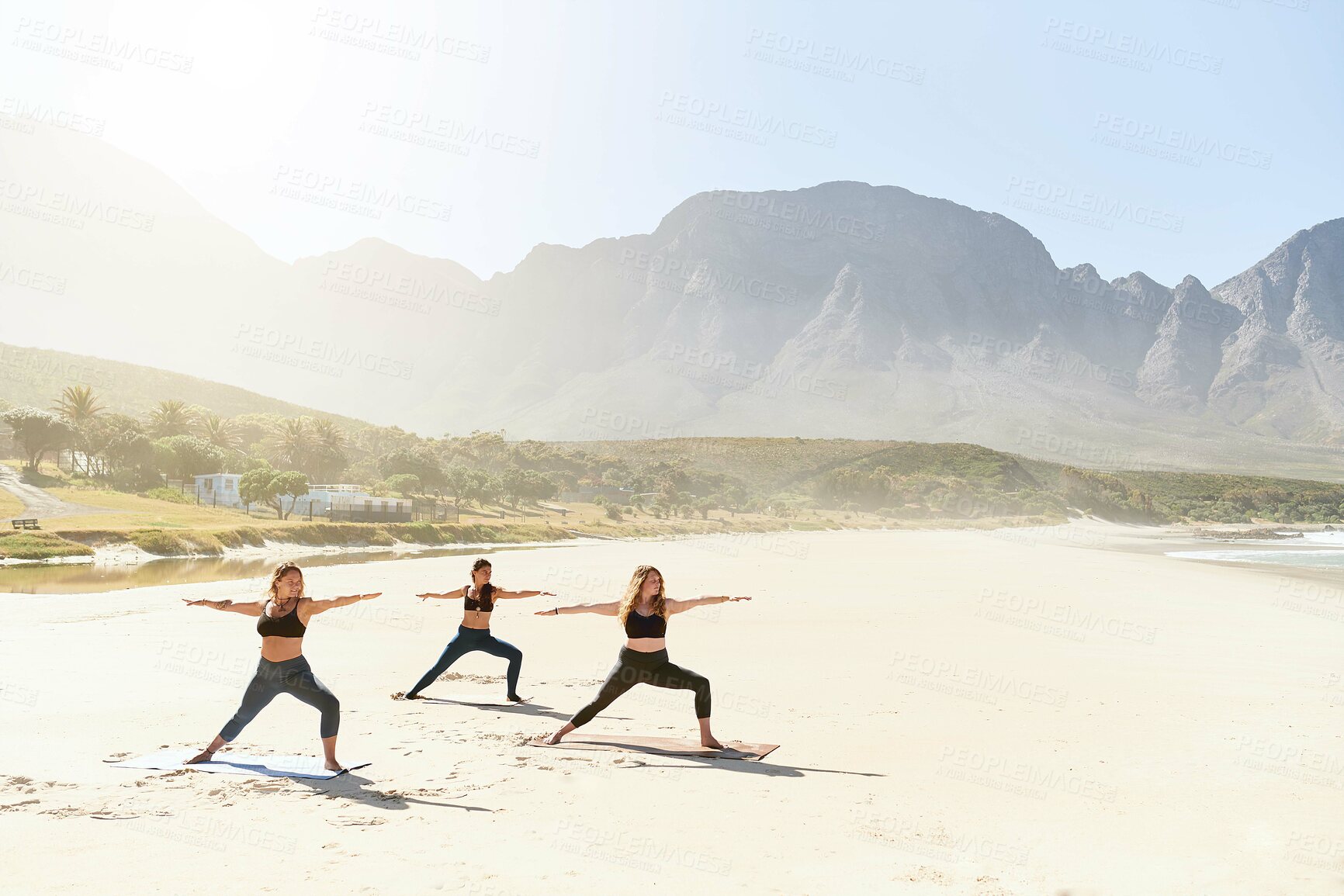 Buy stock photo Warrior pose, yoga and women by ocean for wellness, peace and mindfulness in nature. Morning, pilates and people on beach for exercise, meditation and workout for health, balance and stretching