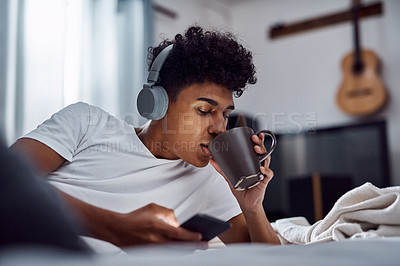 Buy stock photo Drinking coffee, phone and man with headphones for music, morning or scroll on social media to relax. Mobile, tea and person in bed for streaming sound, text message or listen to rock in bedroom home