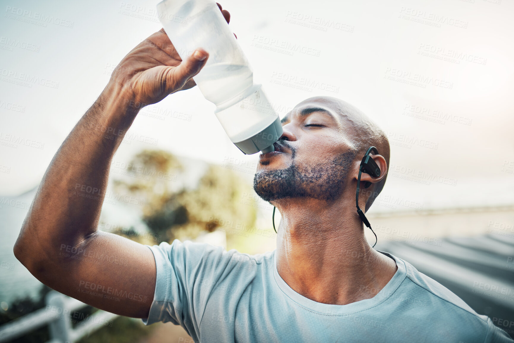 Buy stock photo Drinking water, fitness and bottle with African man and headphones for music or podcast streaming. Outdoor, exercise and hydration drink with liquid, wellness and training with health in Mozambique