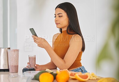 Buy stock photo Woman, smartphone and smoothie drink in home, typing and fruit for mineral liquid in kitchen. Female person, nutrition and online for social media blog on diet, breakfast cocktail and vegan website