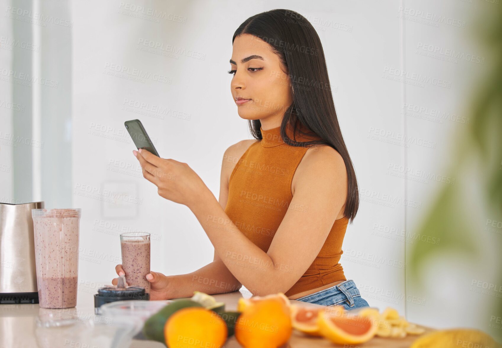 Buy stock photo Woman, smartphone and smoothie drink in home, typing and fruit for mineral liquid in kitchen. Female person, nutrition and online for social media blog on diet, breakfast cocktail and vegan website