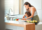 Loving mother and small daughter chopping vegetables and preparing a salad in the kitchen at home. Girl bonding with mother while learning to cook