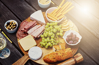 Buy stock photo Wood, wine and cheese on board for picnic buffet, celebration and luxury food in backyard. Bread, meat and fruit for charcuterie snacks on table at outdoor garden party for thanksgiving with drinks