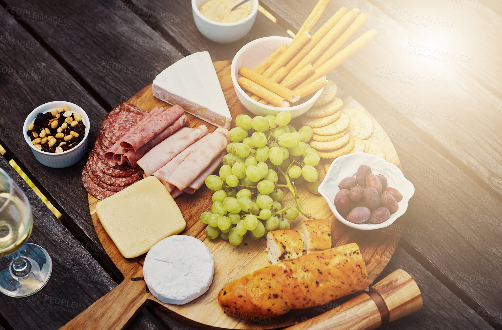 Buy stock photo Wood, wine and cheese on board for picnic buffet, celebration and luxury food in backyard. Bread, meat and fruit for charcuterie snacks on table at outdoor garden party for thanksgiving with drinks