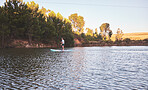 Man standing up on a paddle board on a quiet lake surrounded by trees in nature. Active man enjoying water sports on summer vacation