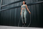 One young african american female athlete skipping using jump rope while exercising outside in the city. Beautiful and dedicated mixed race sportswoman working out alone against an urban background