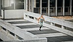 Young mixed race sportswoman looking serious and focused while wearing headphones listening to music and running outside in the city. Exercise is good for your health and wellbeing