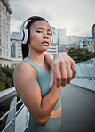 Young mixed race female athlete wearing headphones and listening to music while stretching her muscles before a run outside in the city. Warming up before exercising to improve her health and lifestyle