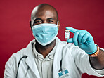 African american covid doctor holding corona vaccine while wearing surgical face mask. Closeup portrait of black physician with drug vial against red studio background with copyspace. Virus protected