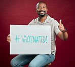 African american covid vaccinated man showing thumbs up sign and symbol and holding poster. Portrait of black man isolated on red studio background with copyspace. Promote corona vaccine and motivate