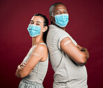 Covid vaccinated African american man and mixed race woman standing back to back. Two people wearing surgical face mask isolated against red background in studio with copyspace. Showing plaster on arm