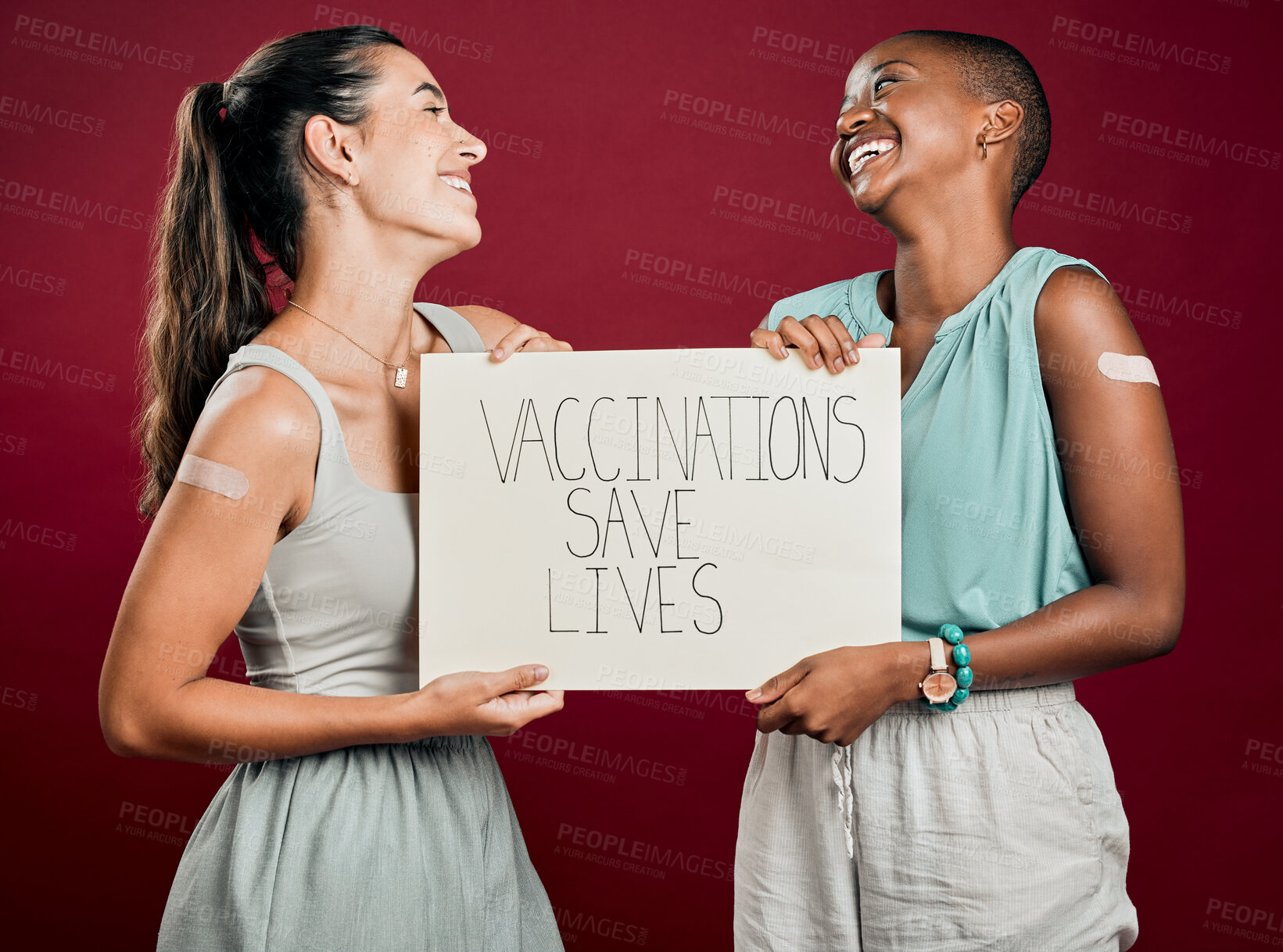 Buy stock photo Laughing, poster and vaccine with happy friends in studio on red background for healthcare or medical. Covid, plaster and vaccination saves lives sign with people together for support or wellness