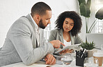 Two mixed race businesspeople working on a digital tablet in a meeting together at work. Business professionals using technology in an office. Businessman pointing to a digital tablet screen while sitting with his female colleague